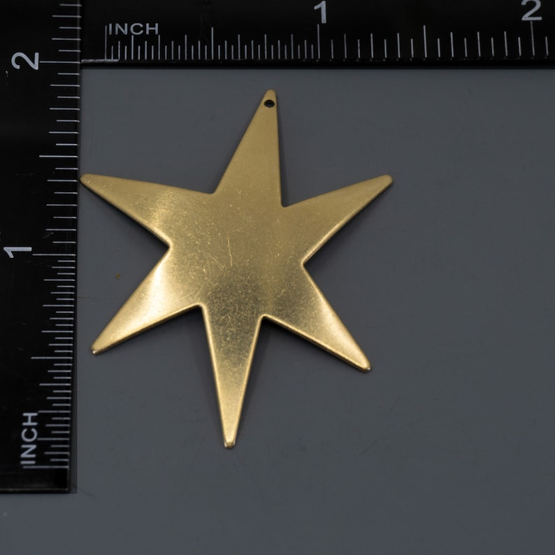 K&ouml;nnte beinhalten: Ein goldfarbener, f&uuml;nfzackiger sternf&ouml;rmiger Anh&auml;nger mit einem Loch oben.
