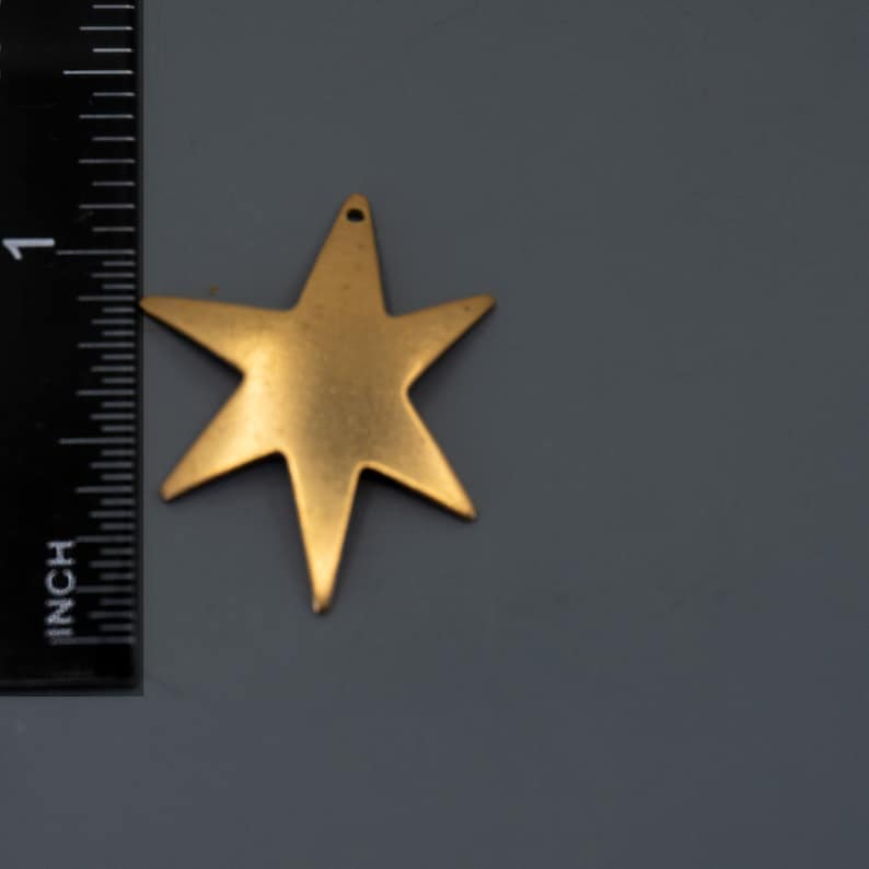 K&ouml;nnte beinhalten: Ein goldfarbener Metall-Stern-Anh&auml;nger mit einem Loch oben zum Aufh&auml;ngen.