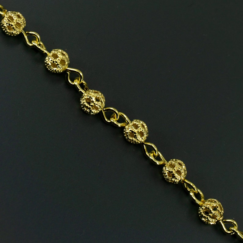 Puede incluir: Un collar de cadena de oro con cuentas redondas caladas. La cadena est&aacute; hecha de peque&ntilde;as piezas de metal unidas.