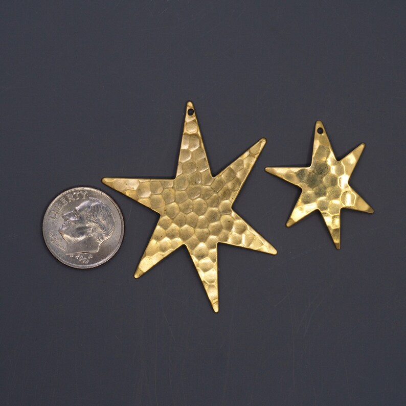 May include: Two gold-toned metal star-shaped charms with a hammered texture. The larger star is about the size of a US quarter.