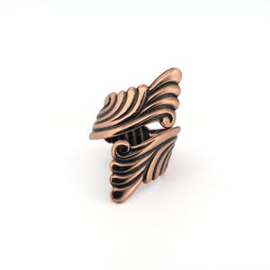 A copper-colored ring with an intricate, swirling design.