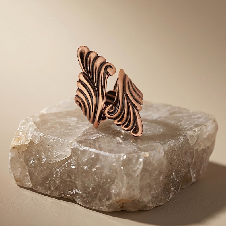 A copper-colored ring with a swirling, organic design sits atop a large, jagged rock formation.