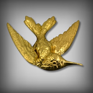 Peut inclure: Une figurine d'oiseau en métal de couleur dorée avec des ailes détaillées et un bec. L'oiseau est en position de vol, les ailes déployées.