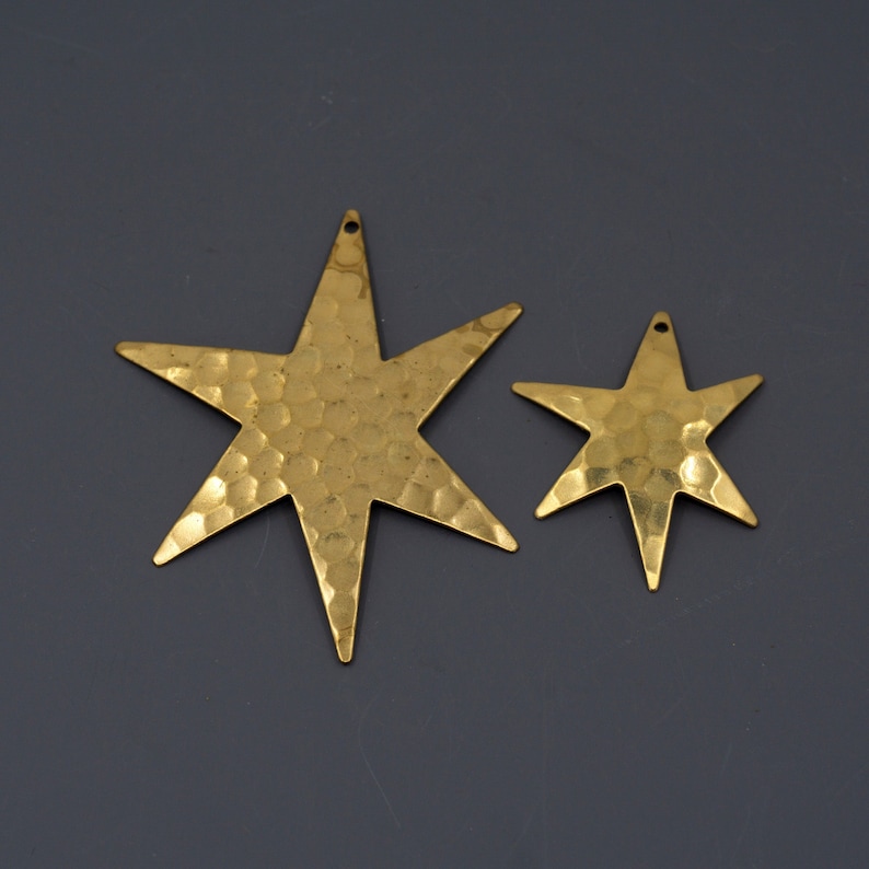 May include: Two gold-toned metal star-shaped charms with a hammered texture. The larger star is about twice the size of the smaller star.