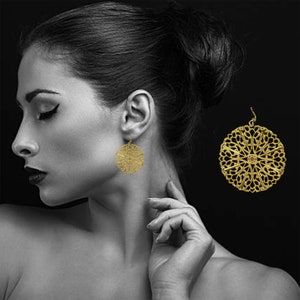 May include: Gold filigree earrings with a circular design. The earrings are dangling and have a delicate, intricate pattern.