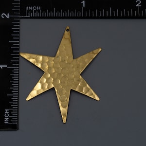 May include: A gold-toned, hammered metal star charm with a six-pointed design. The star is approximately 1 inch in diameter.