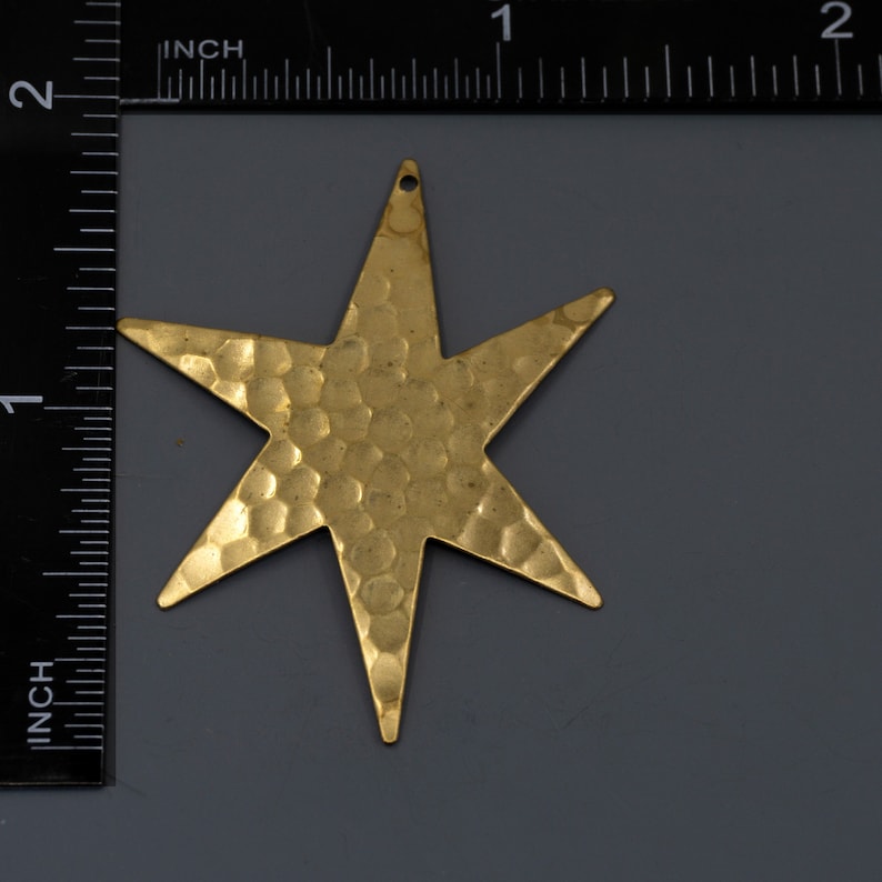 May include: A gold-toned, hammered metal star charm with a six-pointed design. The star is approximately 1 inch in diameter.