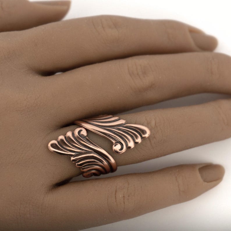 A close-up of a hand wearing a ring with an intricate, wing-like design.