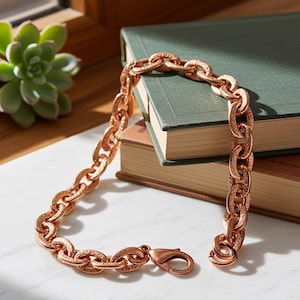 May include: A rose gold-toned chain necklace featuring thick, oval-shaped links with an intricate, embossed pattern on the surface. The necklace includes a lobster claw clasp closure, providing a secure fastening mechanism for the jewelry piece.