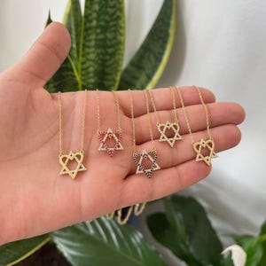 May include: Five gold necklaces with a Star of David pendant. Each pendant is outlined with small clear stones and filled with coloured stones. The pendants are red, blue, black, and two are clear.