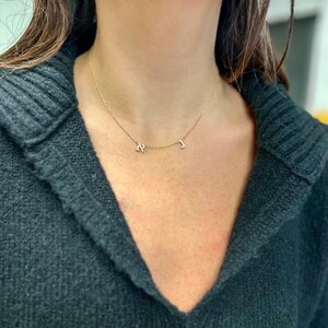 May include: A gold chain necklace with two small, diamond-encrusted letters, "K" and "J", hanging from it.