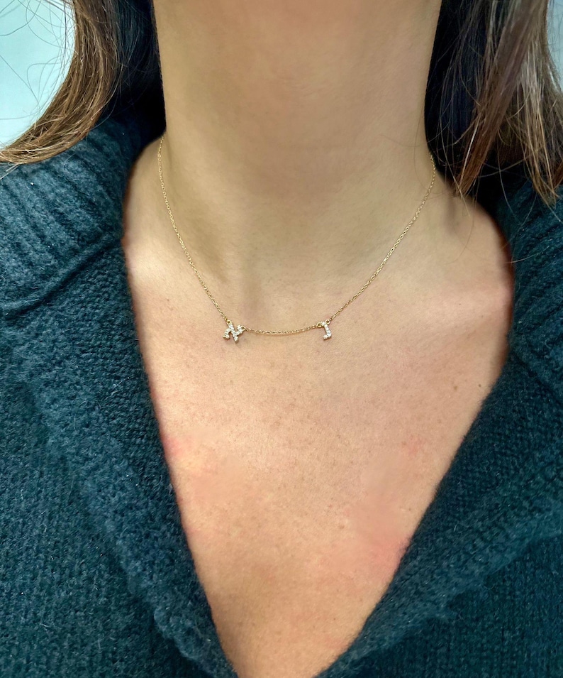 May include: A gold chain necklace with two small diamond-encrusted letters, "N" and "I", hanging from it.