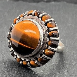May include: A silver ring with a round tiger's eye gemstone set in a beaded bezel.