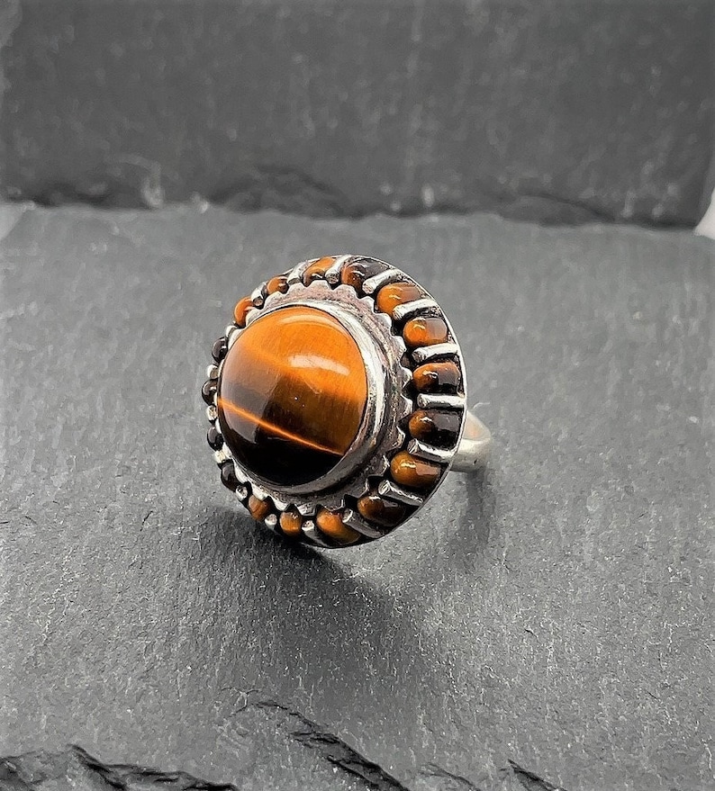 May include: A silver ring with a round tiger's eye gemstone set in a beaded bezel.