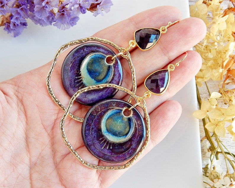 Large gold hoops with a round porcelain charm inside and an amethyst gem on the top of the hoop, the hooks are made of gold wire.