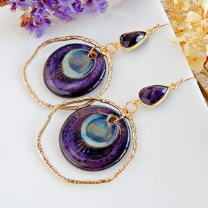 Peut inclure: Boucles d'oreilles cr&eacute;oles dor&eacute;es avec un pendentif en c&eacute;ramique bleu et violet en forme de larme et une goutte de pierre pr&eacute;cieuse violette.