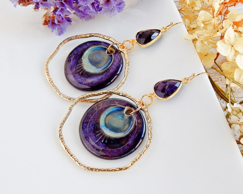 Peut inclure: Boucles d'oreilles cr&eacute;oles dor&eacute;es avec un pendentif en c&eacute;ramique bleu et violet en forme de larme et une goutte de pierre pr&eacute;cieuse violette.