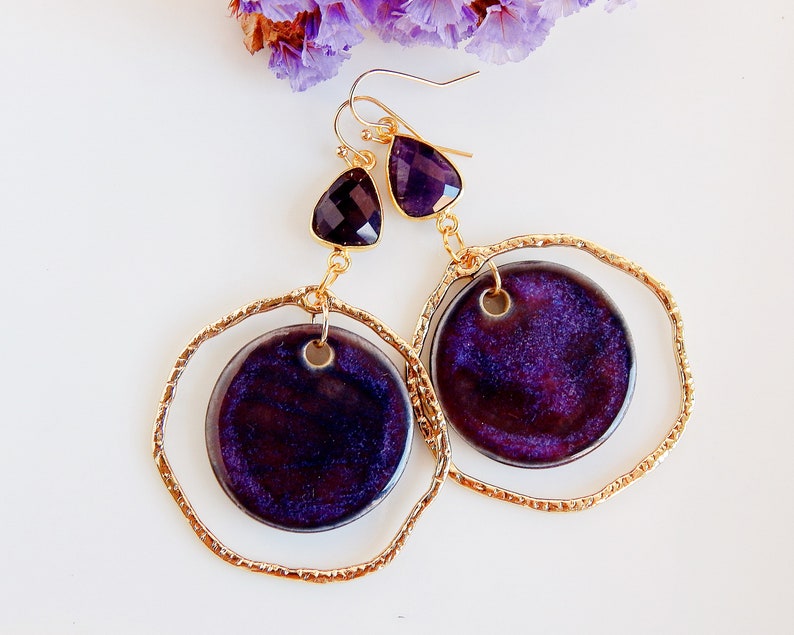 Peut inclure: Une paire de boucles d'oreilles cr&eacute;oles dor&eacute;es avec un pendentif en forme de larme violet et or et un pendentif rond en c&eacute;ramique violet. Le pendentif a une surface textur&eacute;e scintillante.