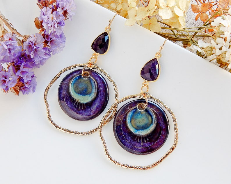 Peut inclure: Boucles d'oreilles violettes et dor&eacute;es avec une pierre pr&eacute;cieuse am&eacute;thyste en forme de larme et un charme rond en c&eacute;ramique avec un motif tourbillonnant.