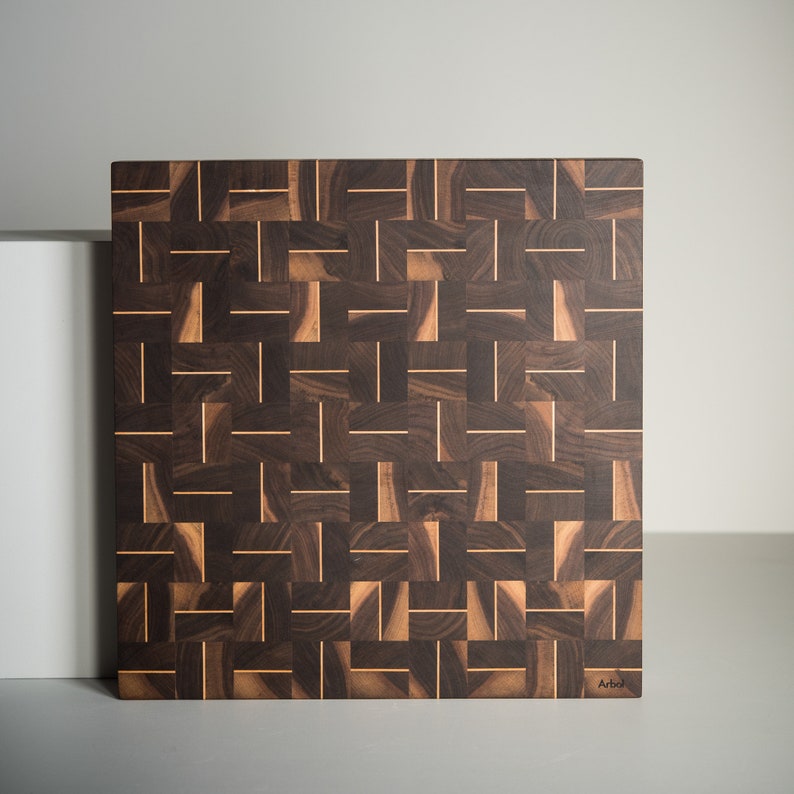 May include: A large, rectangular cutting board made of dark wood with a woven pattern of light wood strips. The board has a "Arbol" logo in the bottom right corner.