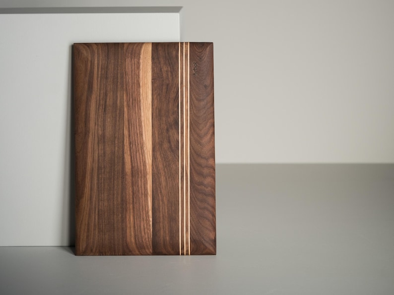 Op de afbeelding: Rechthoekige houten snijplank met een donkerbruine afwerking. Twee dunne, lichtgekleurde strepen lopen verticaal door het midden. De plank is gemaakt van hout en heeft een natuurlijk nerfpatroon.