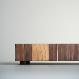 May include: A rectangular wooden cutting board with a light brown center section and dark brown wood on either side. The board has a thin strip of light wood running down the center.