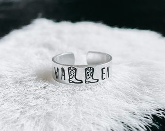 Könnte beinhalten: Ein silberner Ring mit der Gravur "WALLEN" und zwei Cowboystiefeln auf beiden Seiten des Wortes.