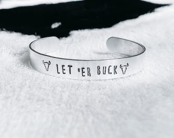 Op de afbeelding: Zilveren armband met de tekst "LET 'ER BUCK" en een stierenkopontwerp aan elke kant.