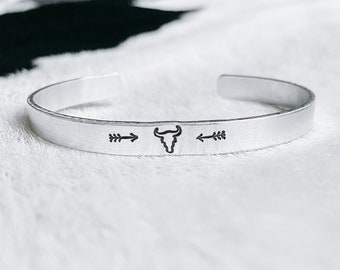 Op de afbeelding: Zilveren armband met een schedel en pijl ontwerp.