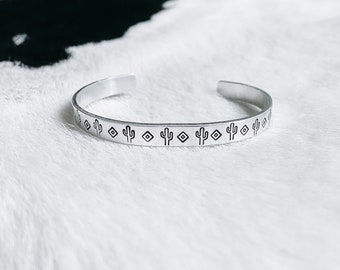 Op de afbeelding: Zilveren armband met een herhalend patroon van kleine cactussen en diamanten.
