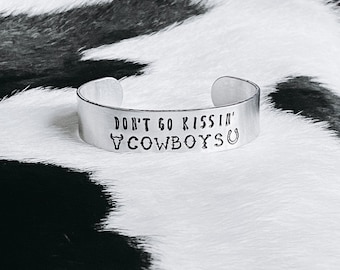 Op de afbeelding: Zilveren armband met de tekst "Don't go kissin' cowboys" en een gestileerde stierenkop en een hoefijzer.