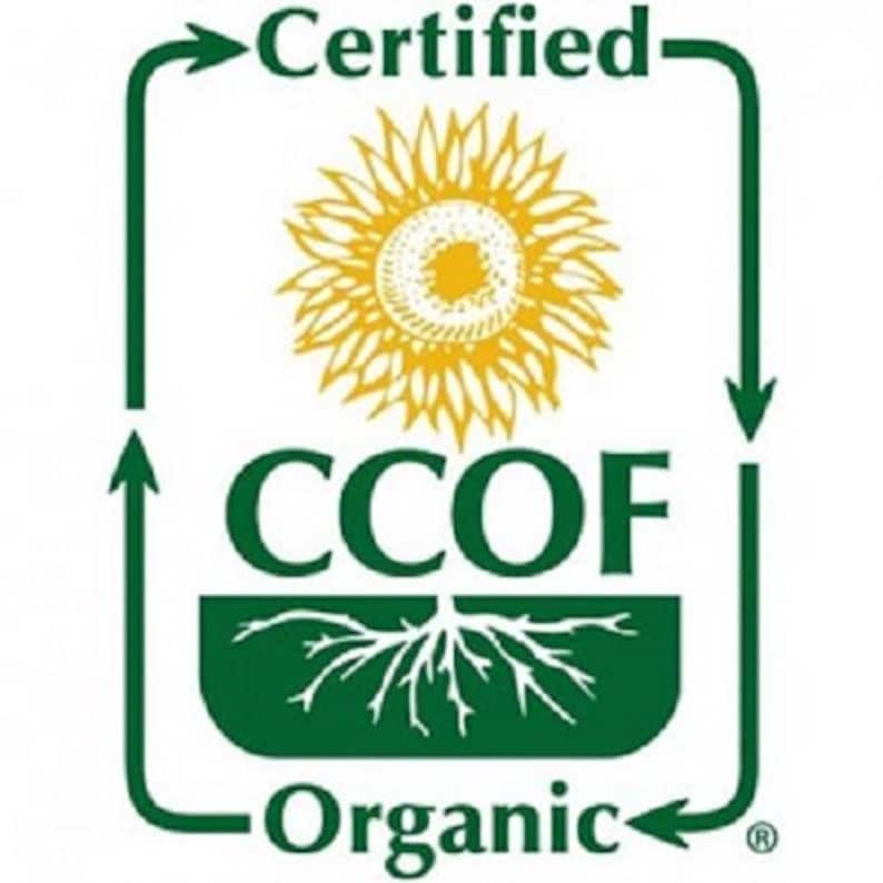 May include: A green and white logo with the words "Certified Organic" and "CCOF". The logo features a yellow sunflower in the center, with a green border that has arrows pointing in a circular direction. The word "Organic" is at the bottom.