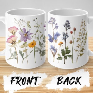 May include: White ceramic mug with a floral design. The front of the mug features a variety of pressed flowers in shades of purple, pink, yellow, and green. The back of the mug features a similar design with blue, purple, and green flowers.