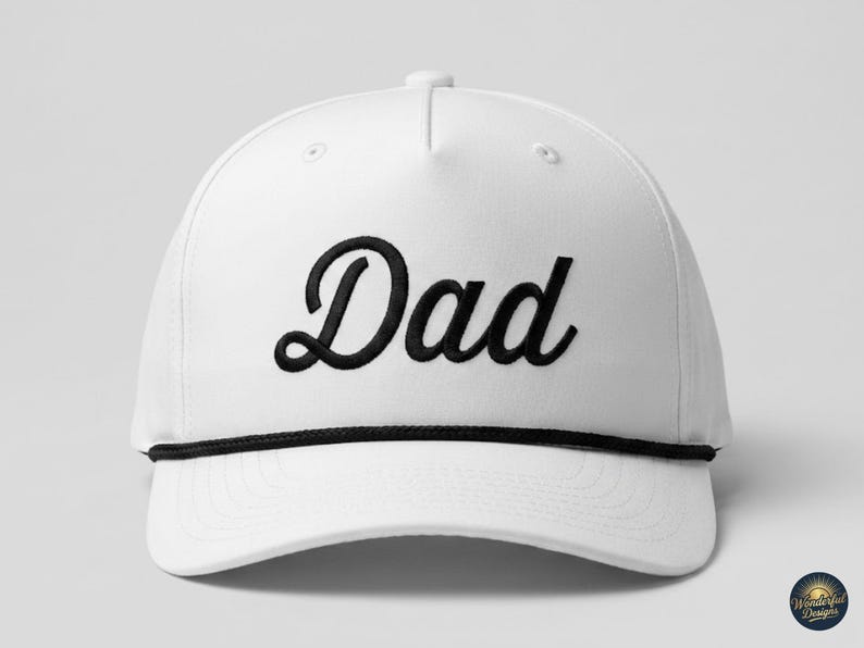Puede incluir: Una gorra de b&eacute;isbol blanca con la palabra Dad bordada en una fuente cursiva negra en el panel frontal. La gorra incluye un detalle de cuerda negra que recorre horizontalmente la base de la corona, justo encima de la visera curva y estructurada.