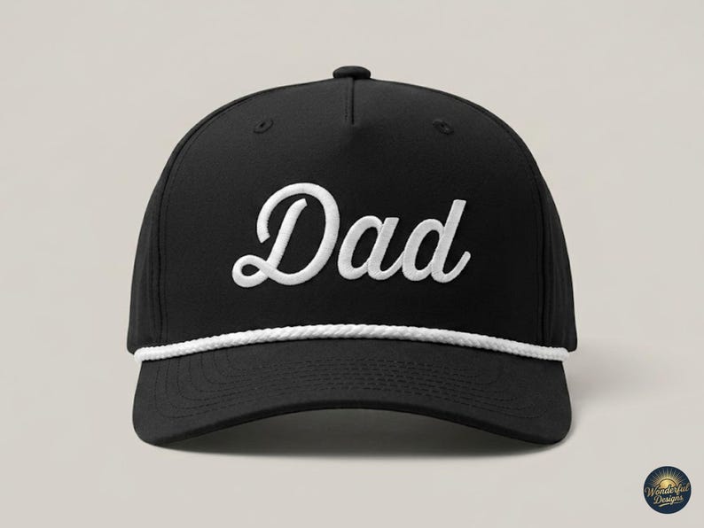 Puede incluir: Una gorra de b&eacute;isbol negra con la palabra Dad bordada en fuente cursiva blanca en el panel frontal. La gorra incluye un detalle de cuerda trenzada blanca que recorre horizontalmente la base de la corona, justo encima de la visera curva.