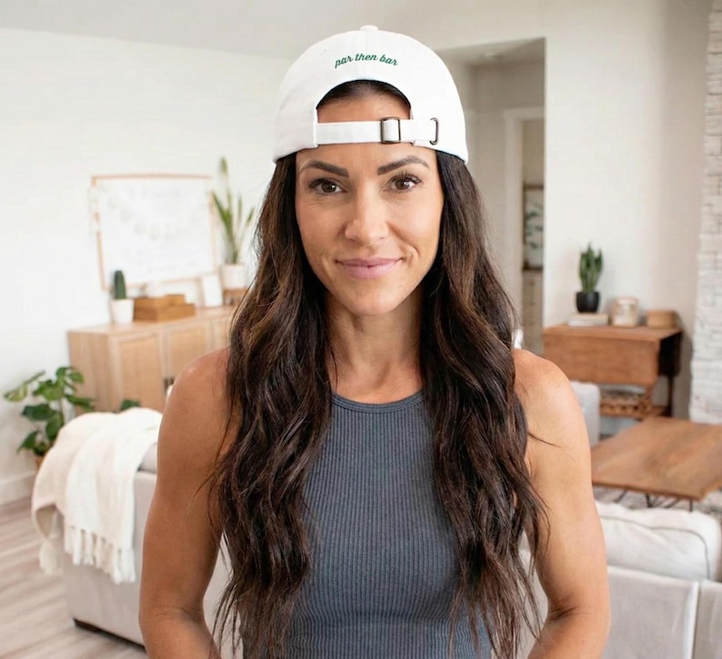May include: A white baseball cap with the text "par then bar" embroidered in green. The cap has a curved brim and an adjustable strap. The person is wearing a gray tank top.