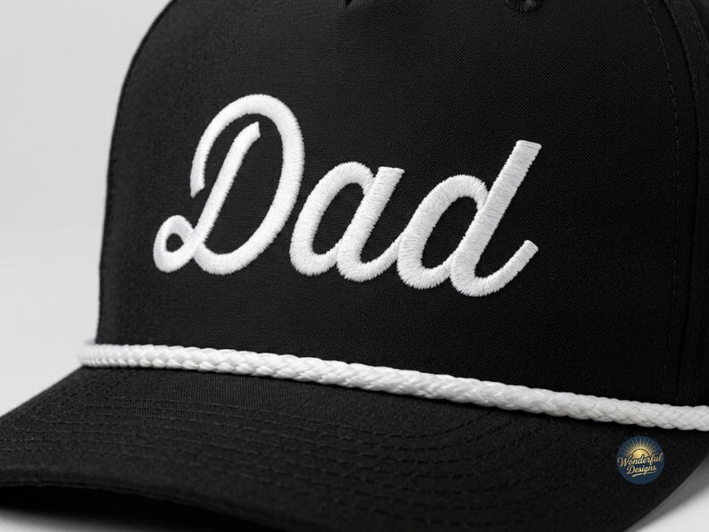 Puede incluir: Una gorra de b&eacute;isbol negra con la palabra Dad bordada en letra cursiva blanca en el panel frontal. La gorra incluye un detalle de cord&oacute;n trenzado blanco colocado horizontalmente en la base de la corona, justo encima de la visera.