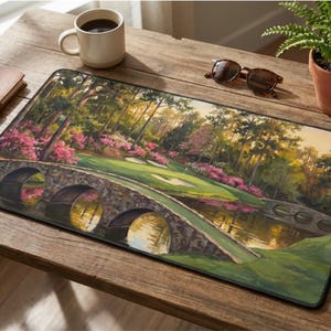 May include: A rectangular mousepad featuring a scenic golf course landscape with a stone bridge, water, and vibrant pink flowers. The image is a painting with a green golf course and trees.