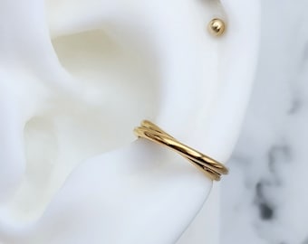 May include: Gold ear cuff with a twisted design, worn on a white mannequin ear. The ear also has three gold stud earrings with clear gemstones.