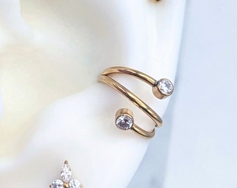 Op de afbeelding: Gouden oor-kraakbeen sieraden met heldere zirkonia stenen. De sieraden omvatten een helix hoepel met twee stenen, een conch ring met twee stenen, een forward helix stud met één steen en twee oorlel studs, één met één steen en de andere met een bloemmotief.