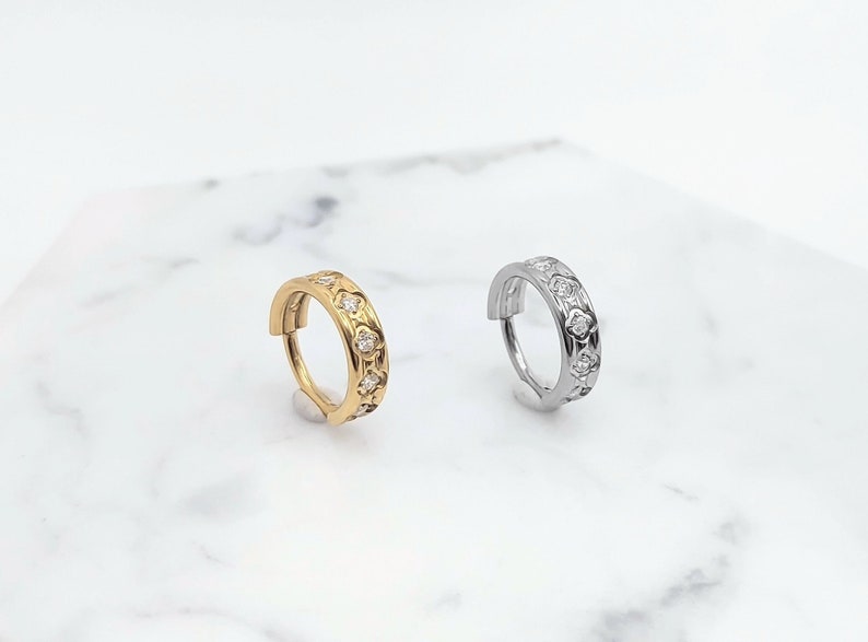 K&ouml;nnte beinhalten: Zwei Creolen mit einem dekorativen Design mit kleinen, klaren Steinen. Die Creole links ist golden und die Creole rechts ist silber.