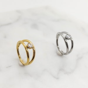 May include: Two gold and silver rings with a single clear stone set in the center. The rings are double-banded and have a simple, modern design.