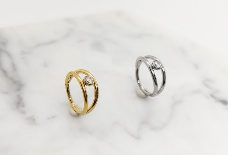 May include: Two gold and silver rings with a single clear stone set in the center. The rings are double-banded and have a simple, modern design.