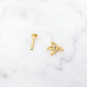 Puede incluir: Joyer&iacute;a corporal de oro con un peque&ntilde;o dise&ntilde;o de flor y una gema transparente en el centro.