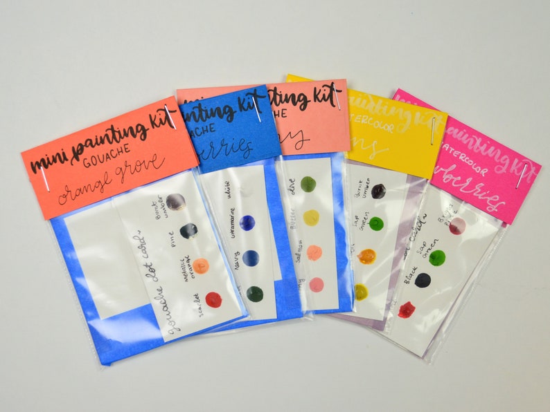 May include: Five mini painting kits with different color palettes. Each kit includes a small plastic bag with a card showing the colors and a label with the name of the kit. The kits are labeled "mini painting kit gouache orange grove", "mini painting kit gouache berries", "mini painting kit the sky", "mini painting kit watercolor lemons", and "mini painting kit watercolor berries".
