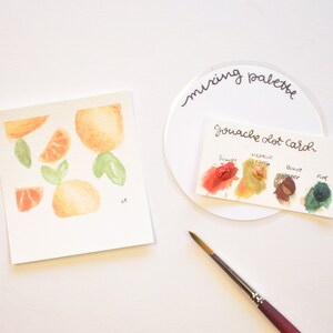 May include: A watercolor painting of oranges and leaves on a white card. A mixing palette with a gouache dot card showing four colors: scarlet, metallic cream, burnt umber, and pine.