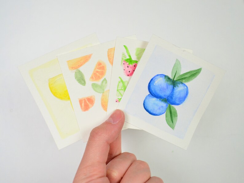 May include: Four watercolor paintings on white cardstock. The paintings depict a lemon, orange slices, strawberries, and blueberries.