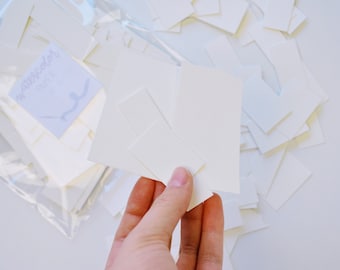 Könnte beinhalten: Nahaufnahme einer Hand, die einen Stapel weißen Aquarellpapiers hält. Das Papier befindet sich in einem durchsichtigen Plastikbeutel mit der Aufschrift "Aquarellpapier".