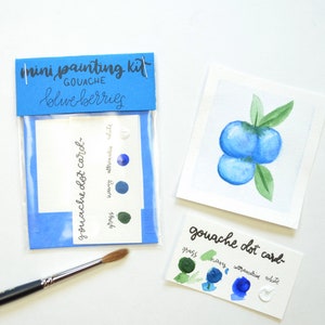 May include: A mini painting kit for creating watercolor blueberries. The kit includes a small card with paint swatches for grass, navy, ultramarine, and white, and a larger card with a watercolor painting of blueberries.