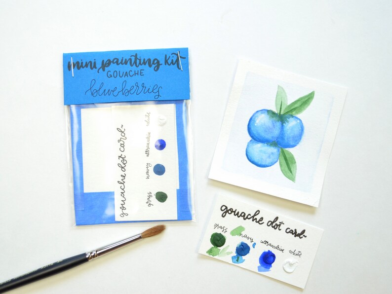 May include: A mini painting kit for creating watercolor blueberries. The kit includes a small card with paint swatches for grass, navy, ultramarine, and white, and a larger card with a watercolor painting of blueberries.